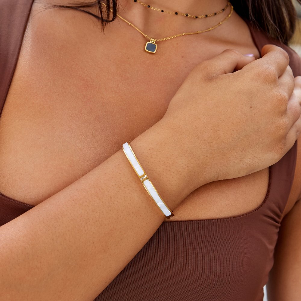 White Sahara Gold Bangle, worn on a wrist with a gold necklace and brown top